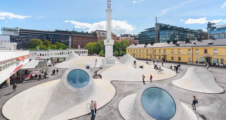 Een modern plein met unieke architectonische structuren en wandelende mensen.