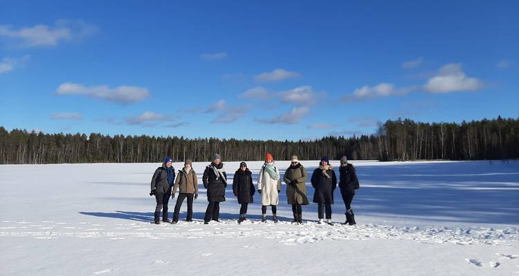 Groep mensen die op een bevroren meer staat met bos op de achtergrond.
