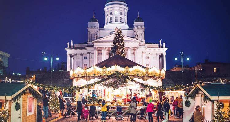 Feestelijk versierd plein met een carrousel en mensen in winterkleding, voor een gebouw met koepel.
