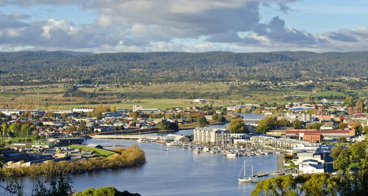 Stadshorizon met rivier en glooiende heuvels op de achtergrond.