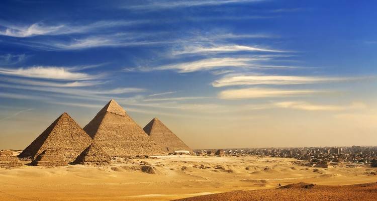 Pyramides de Gizeh avec premier plan désertique et horizon urbain.