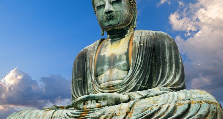 Groot Boeddhabeeld met een bewolkte blauwe lucht op de achtergrond.