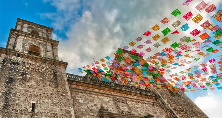 Fachada de iglesia de piedra en Valladolid adornada con coloridas banderas de papel picado ondeando arriba.
