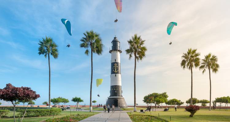 Weißer und schwarzer Leuchtturm im Miraflores-Park von Lima mit mehreren bunten Gleitschirmen, die über dem Park fliegen