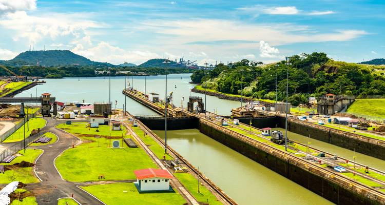 Vista panorámica de las esclusas del Canal de Panamá con barcos pasando a través y colinas exuberantes a lo lejos.
