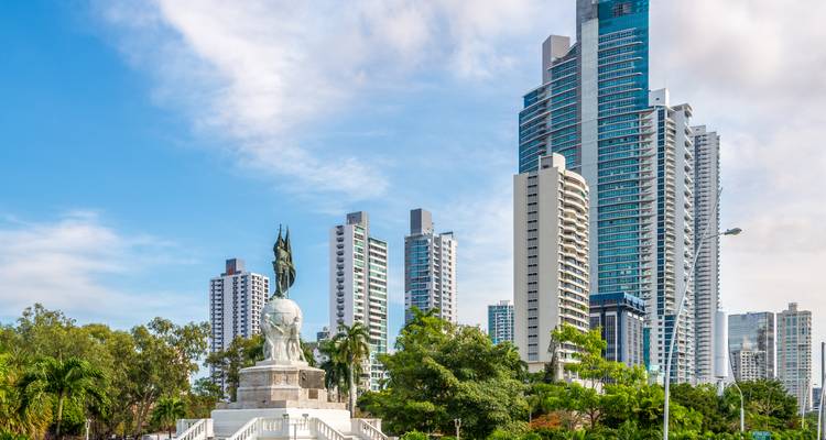 Moderno horizonte de rascacielos de la Ciudad de Panamá detrás de una estatua heroica y exuberante vegetación.