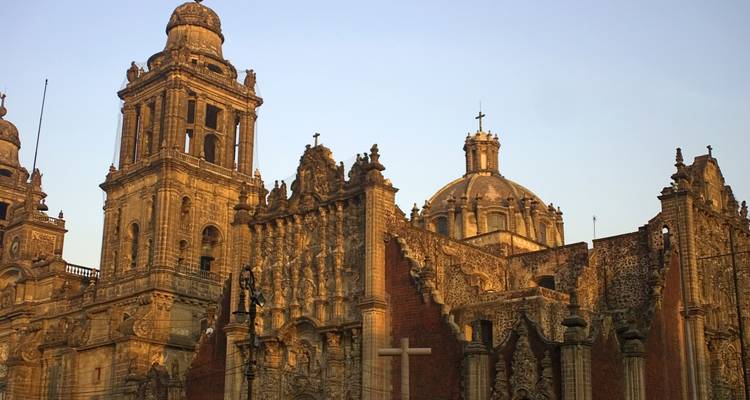 Fachada de piedra y cúpulas de la Catedral Metropolitana de la Ciudad de México brillando con la cálida luz del atardecer.