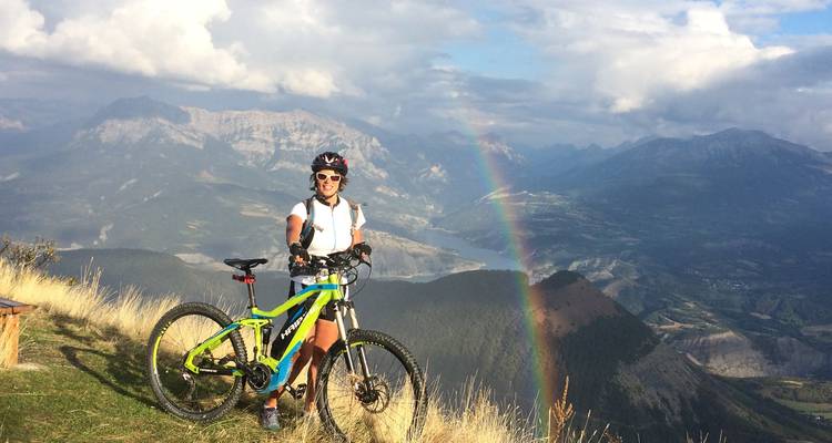 Radfahrer mit einem Regenbogen im Hintergrund auf einem Bergpfad.