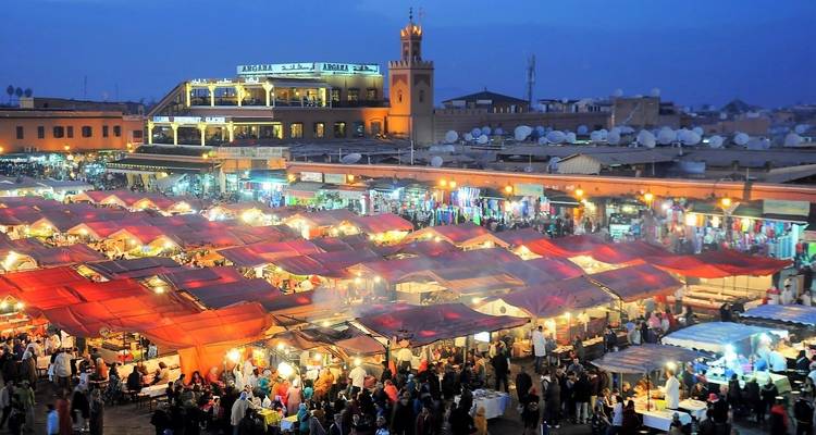 Eine lebhafte Marktszene mit bunten Ständen und Menschen in Marrakesch bei Nacht.