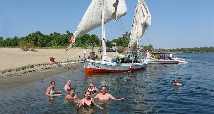 Mensen die zwemmen in een rivier met traditionele zeilboten in de buurt.