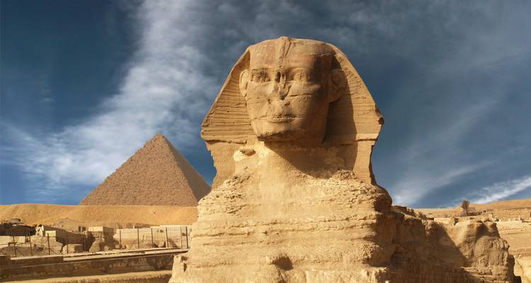 Die Sphinx mit einer Pyramide im Hintergrund unter blauem Himmel.