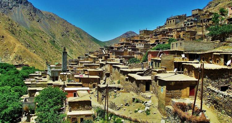 Village à flanc de colline avec maisons en terrasses et verdure.