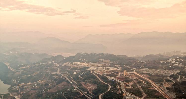 Vista de un amanecer brumoso con capas de crestas montañosas y una ciudad valle extendida parcialmente oculta por la niebla matutina.