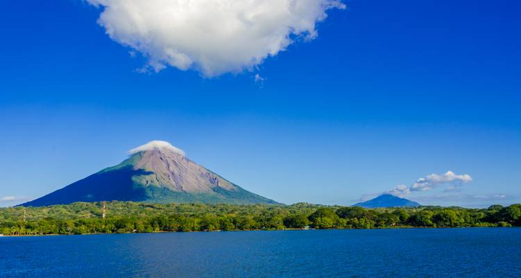 Volcano overlooking a lake with a blue sky and fluffy clouds.