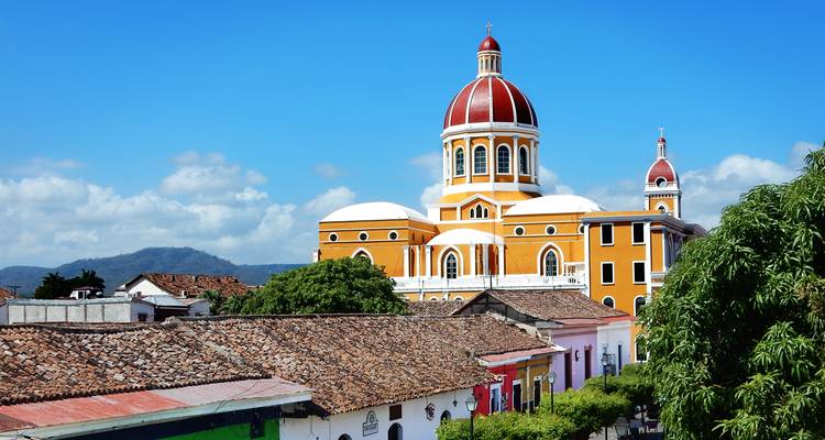 Bright yellow Granada Cathedral towers above colonial tile rooftops against blue sky.