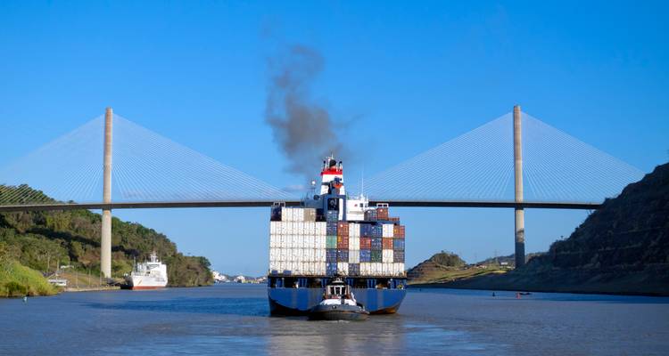 Large container ship transits the Panama Canal beneath a modern cable-stayed bridge.