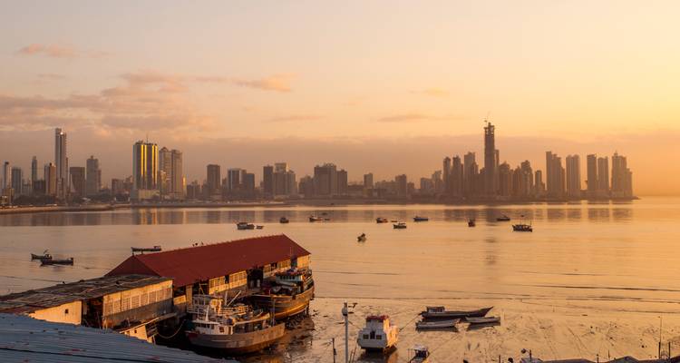 Silhouetted skyline of Panama City reflected on calm bay during golden sunrise.