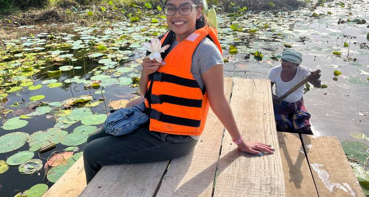 A woman holding a flower wearing a life jacket seated on a dock.