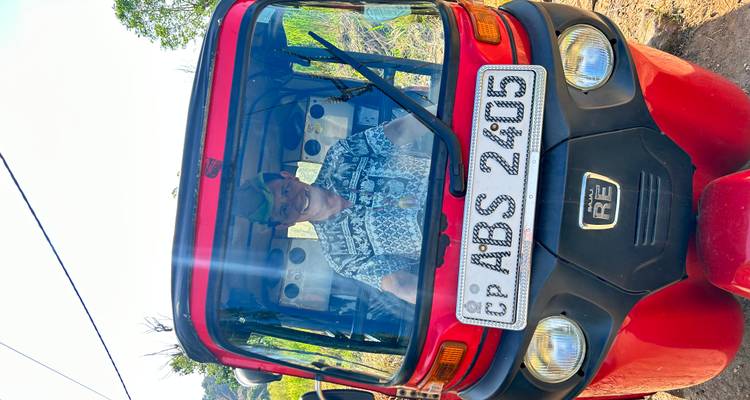 A man inside a tuk-tuk vehicle on a sunny day.
