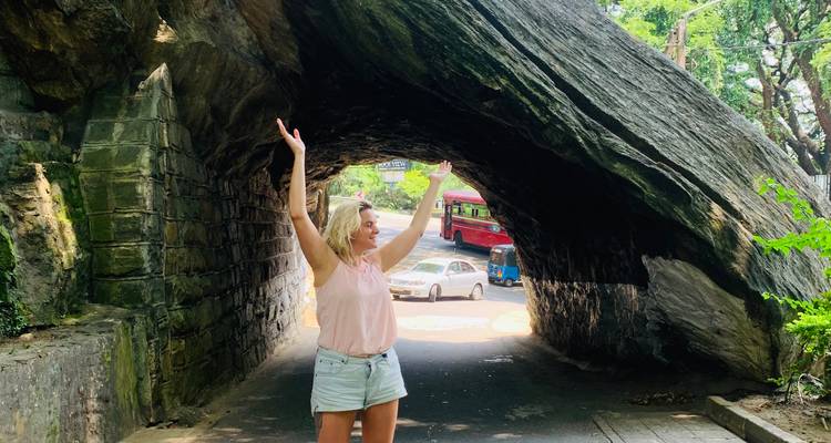 A woman posing under a rock arch in a scenic area.