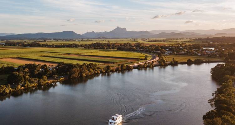Landschap met een rivier, velden en bergen in de verte bij schemering.