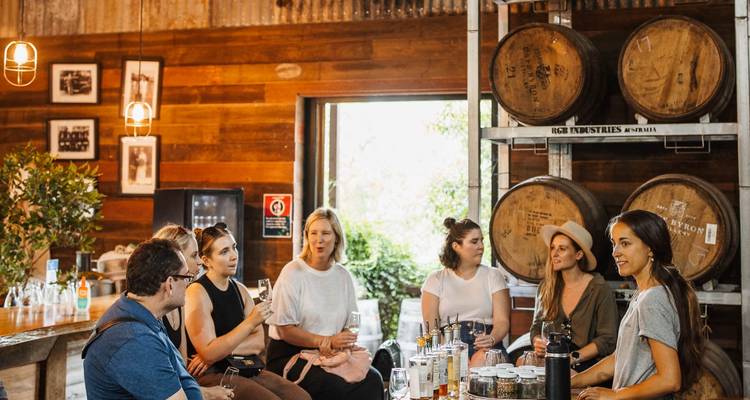 Groep mensen die in een wijnmakerij zitten met vaten op de achtergrond.