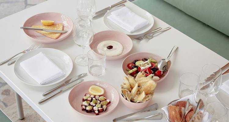 Tafel gedekt met borden met eten en glazen.