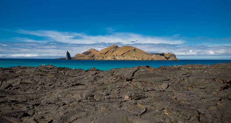 Campo de lava accidentado en primer plano con la distintiva Roca Pinnacle e Isla Bartolomé elevándose desde aguas turquesas.