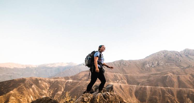 Excursionista emocionado en la cima de un afloramiento rocoso con vista a un cañón.