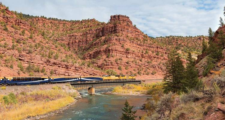 Zug fährt durch eine rote Felsenschlucht entlang eines Flusses.
