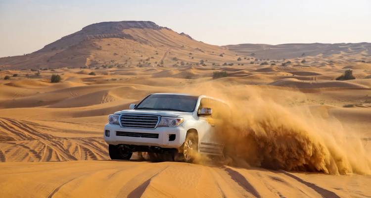 Ein weißer Geländewagen wirbelt eine riesige Sandfahne auf, während er beim Dune Bashing über goldene Dünen in der Nähe von Dubai fährt.