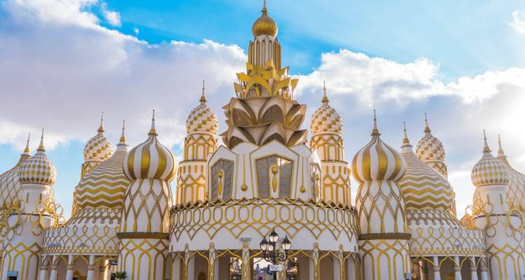 Hell erleuchteter Zwiebeldach-Pavillon des Global Village von Dubai gegen einen blauen Himmel mit zerstreuten Wolken.