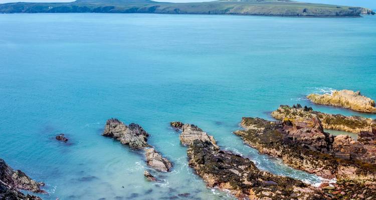Costa galesa rocosa con agua turquesa y acantilados dentados que se extienden hacia el mar tranquilo.