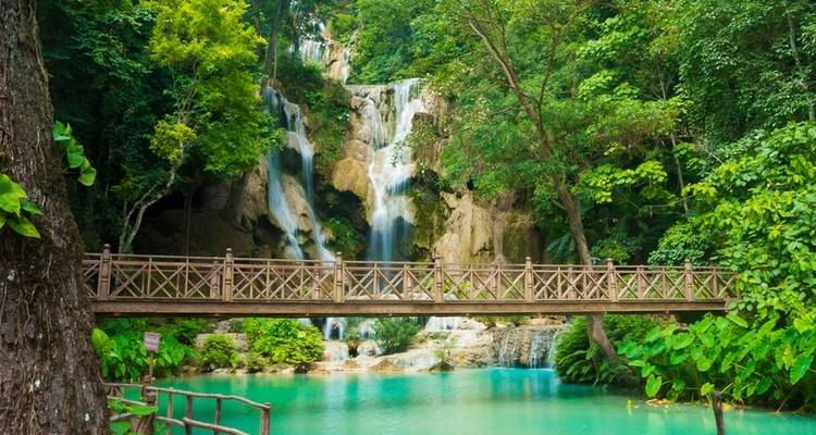 Scenic waterfall with a wooden bridge crossing turquoise waters.
