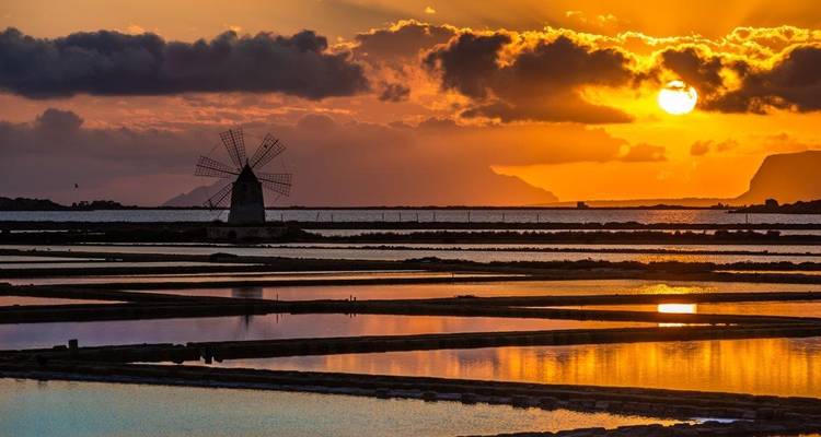 Vue pittoresque de marais salants avec un moulin à vent et un ciel de coucher de soleil.