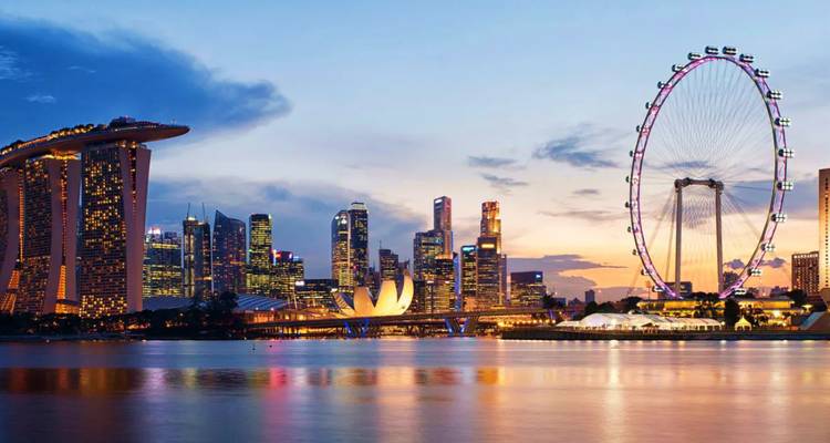 Skyline von Singapur in der Abenddämmerung mit dem Marina Bay Sands, dem Riesenrad Singapore Flyer und Wolkenkratzern, die sich während eines farbenfrohen Sonnenuntergangs in der Bucht spiegeln.