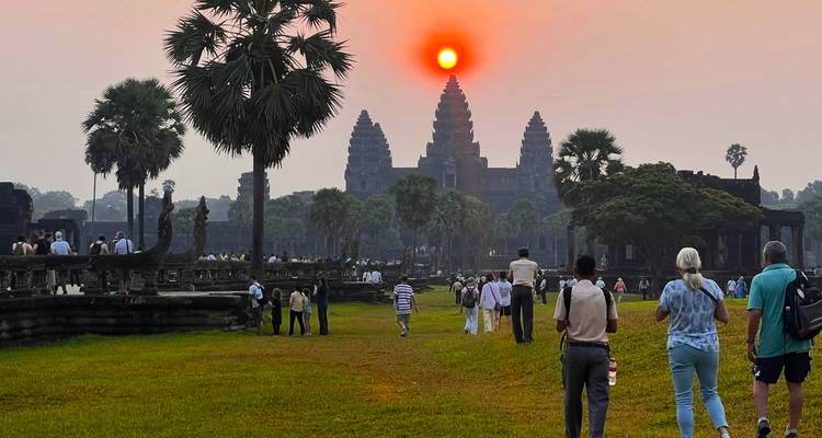 Zon die ondergaat boven de iconische Angkor Wat tempel met bezoekers op de voorgrond