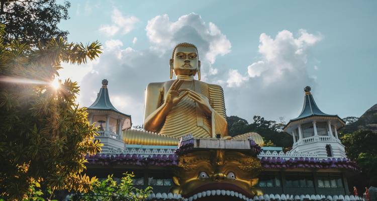 Une grande statue dorée de Bouddha avec des temples dans un cadre luxuriant.