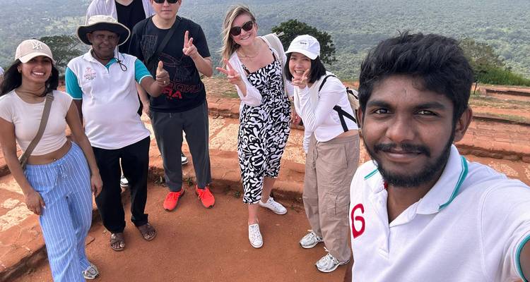 Selfie von fröhlichen Reisenden, die auf einem felsigen Plateau stehen, mit einer weiten grünen Landschaft, die sich darunter erstreckt.