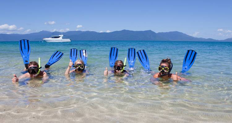 Quatre personnes faisant de la plongée avec tuba dans des eaux bleues claires, avec un ciel bleu éclatant and des montagnes.