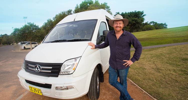 Un homme souriant debout à côté d'une camionnette blanche dans un parc.