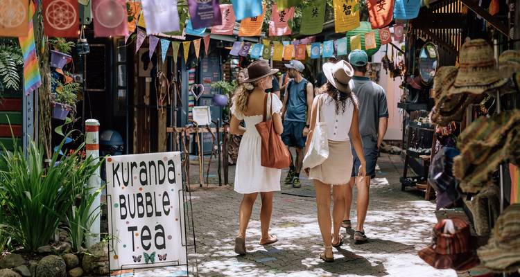 Drie reizigers met zomerpetten bladeren door de kleurrijke marktstraatjes van het dorpje Kuranda.