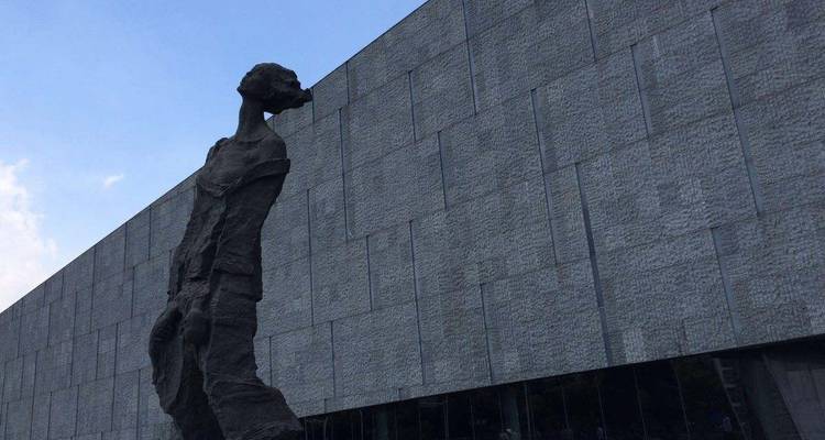 Modern sculpture in front of a large, textured building.