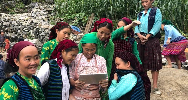 Gruppe von Menschen in traditioneller Kleidung, die auf ein Tablet schauen.
