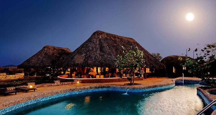 Lodges de luxe aux toits de chaume avec une piscine la nuit.