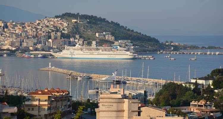 Haven met een groot cruiseschip aangemeerd en een stad op een heuvel op de achtergrond.