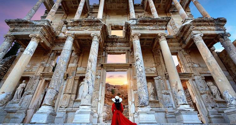 Persoon in rode jurk staat voor grootse oude ruïnes bij zonsondergang.