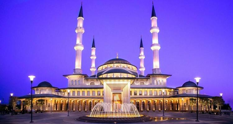 Moskee verlicht in blauw licht tijdens de avond met fonteinen op de voorgrond.