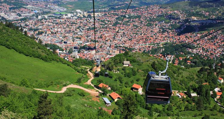 Luftseilbahnen über einer Stadt mit Bergen in der Ferne.