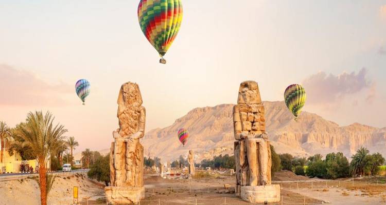 Zwei riesige Statuen mit Heißluftballons am Himmel.